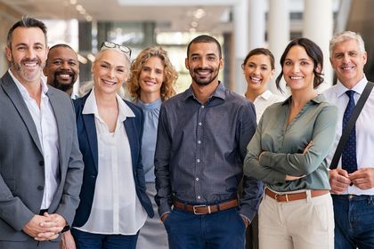 Group of smiling professionals standing together in a bright office hallway