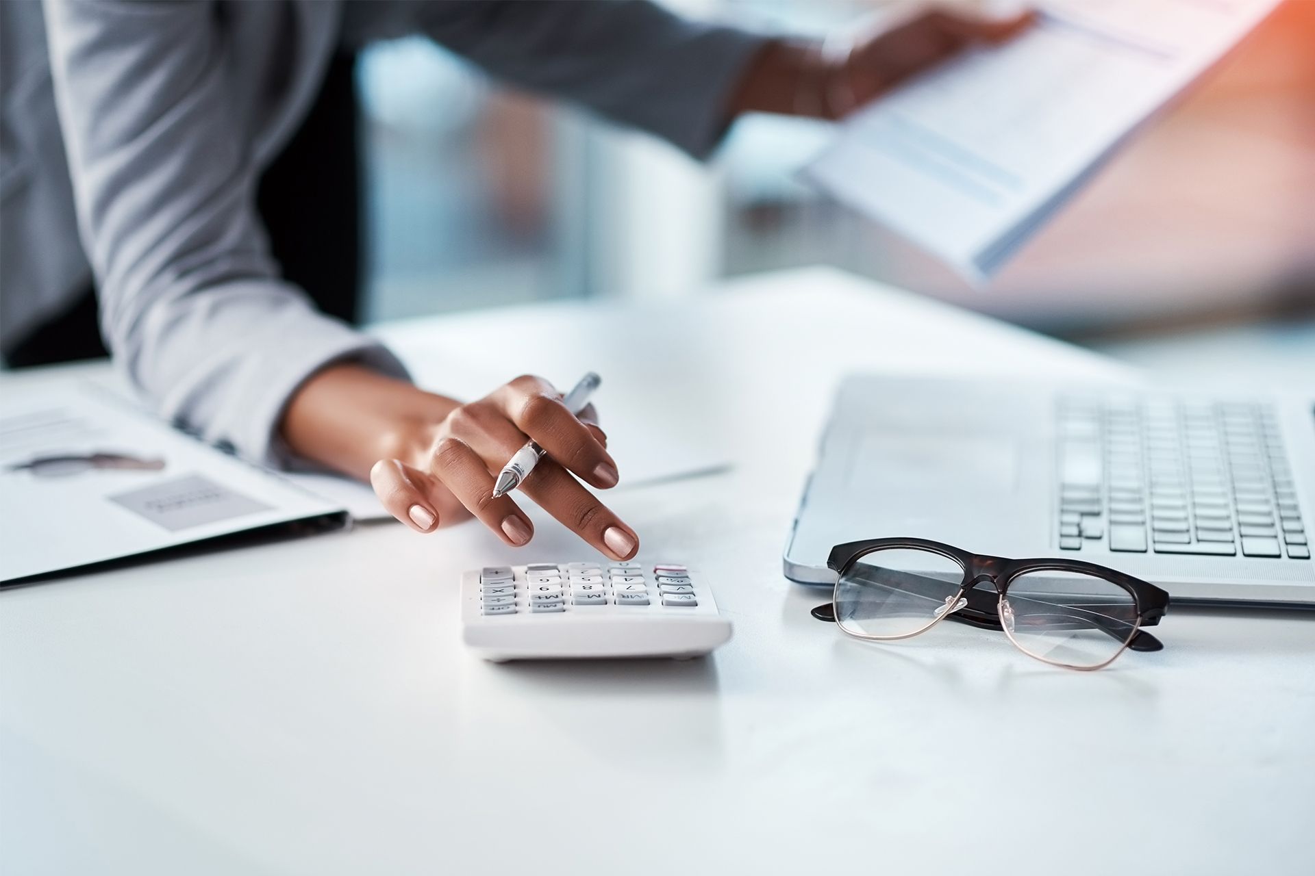Person using calculator beside laptop and eyeglasses on a desk