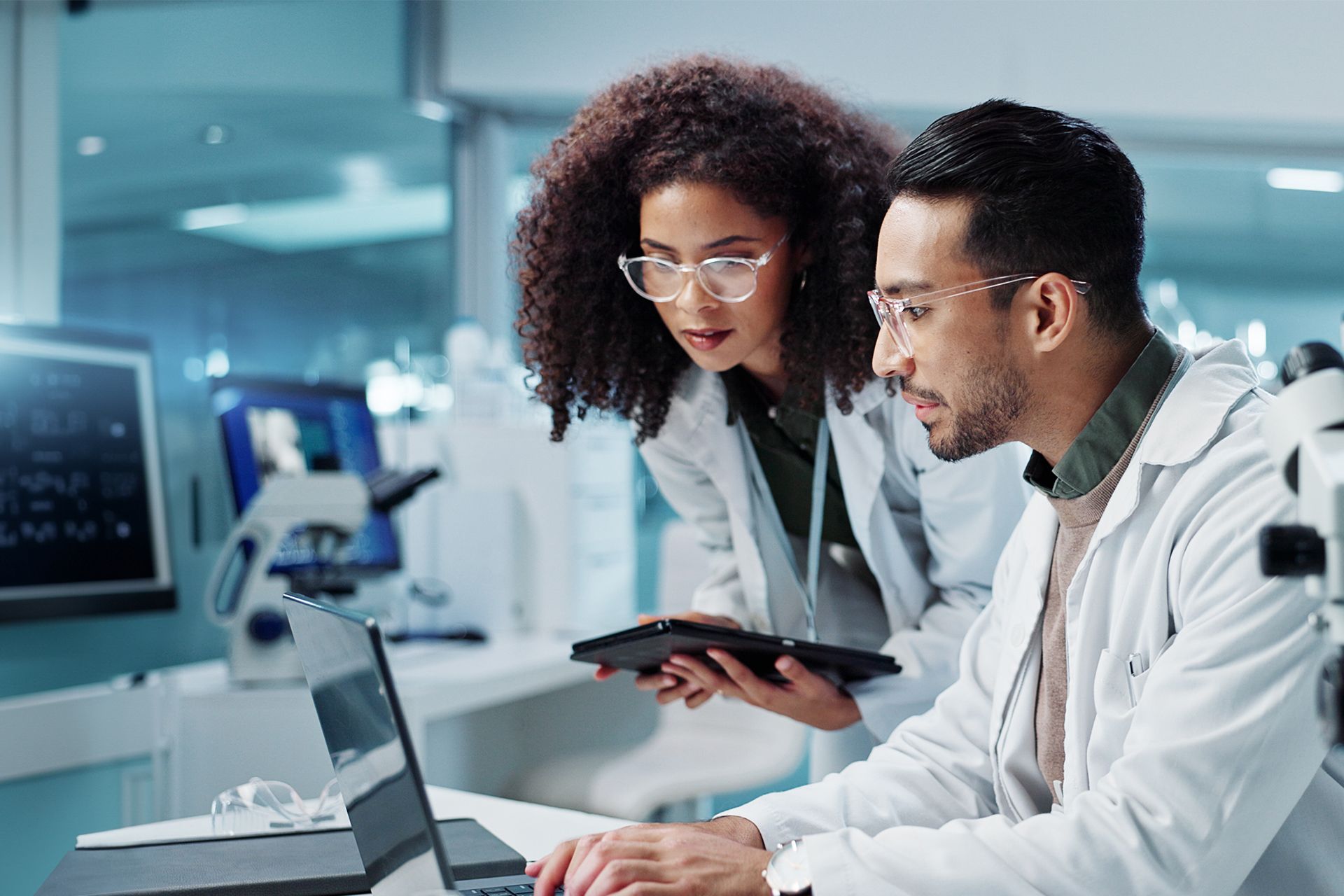 Two clinicians review data on a laptop and tablet in a bright modern lab office.