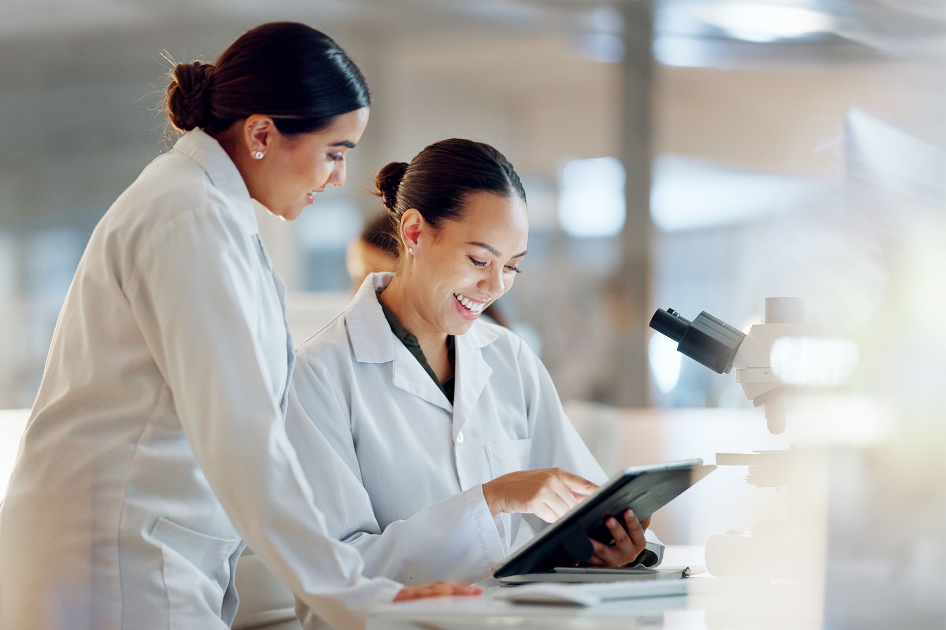 Two scientists in white lab coats reviewing data on a tablet in a bright laboratory