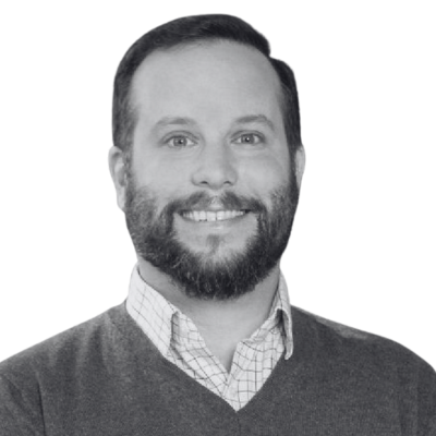 Smiling bearded man in a gray sweater over a checkered shirt against a white background