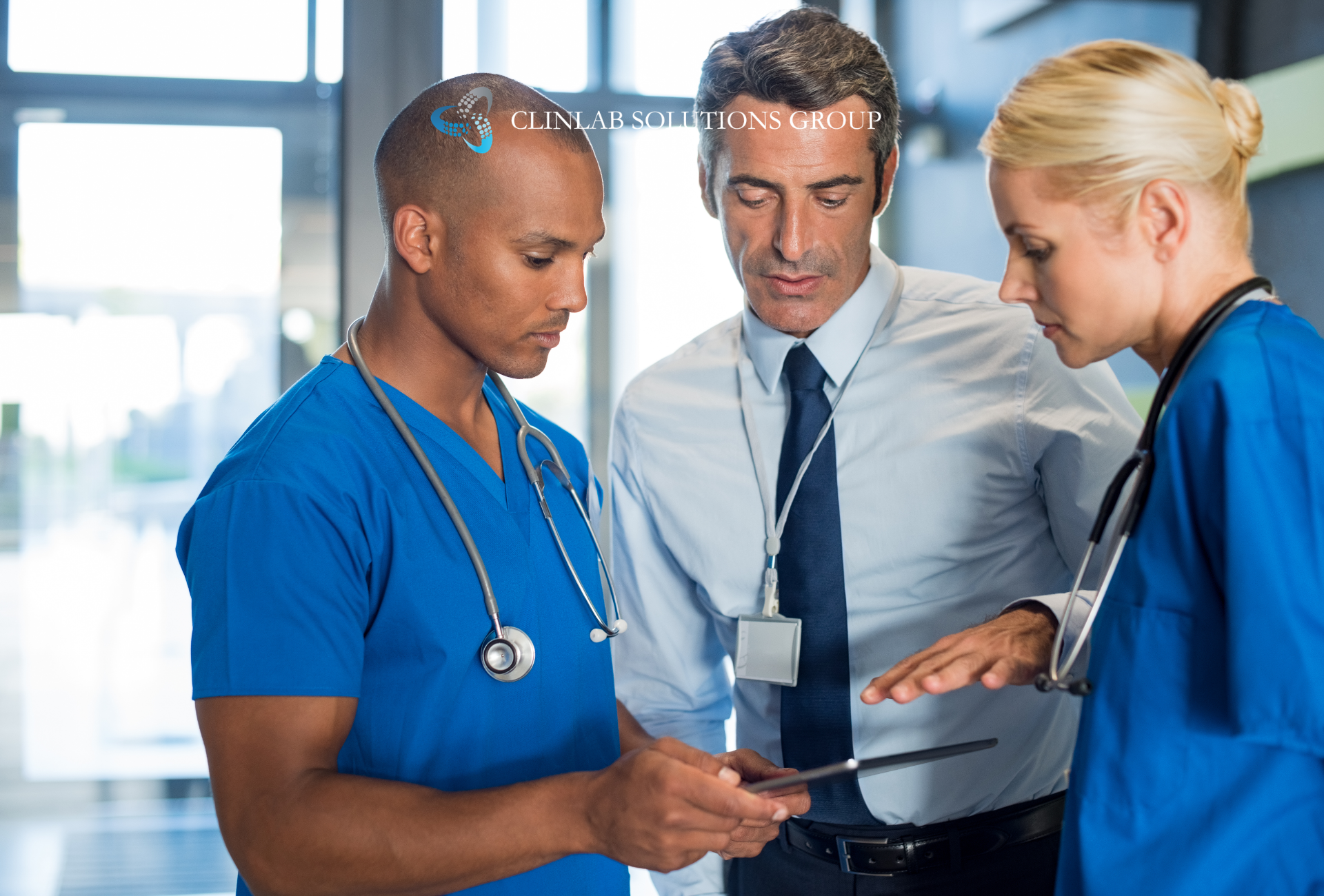 Three clinical research professionals reviewing data on a tablet in a hospital corridor