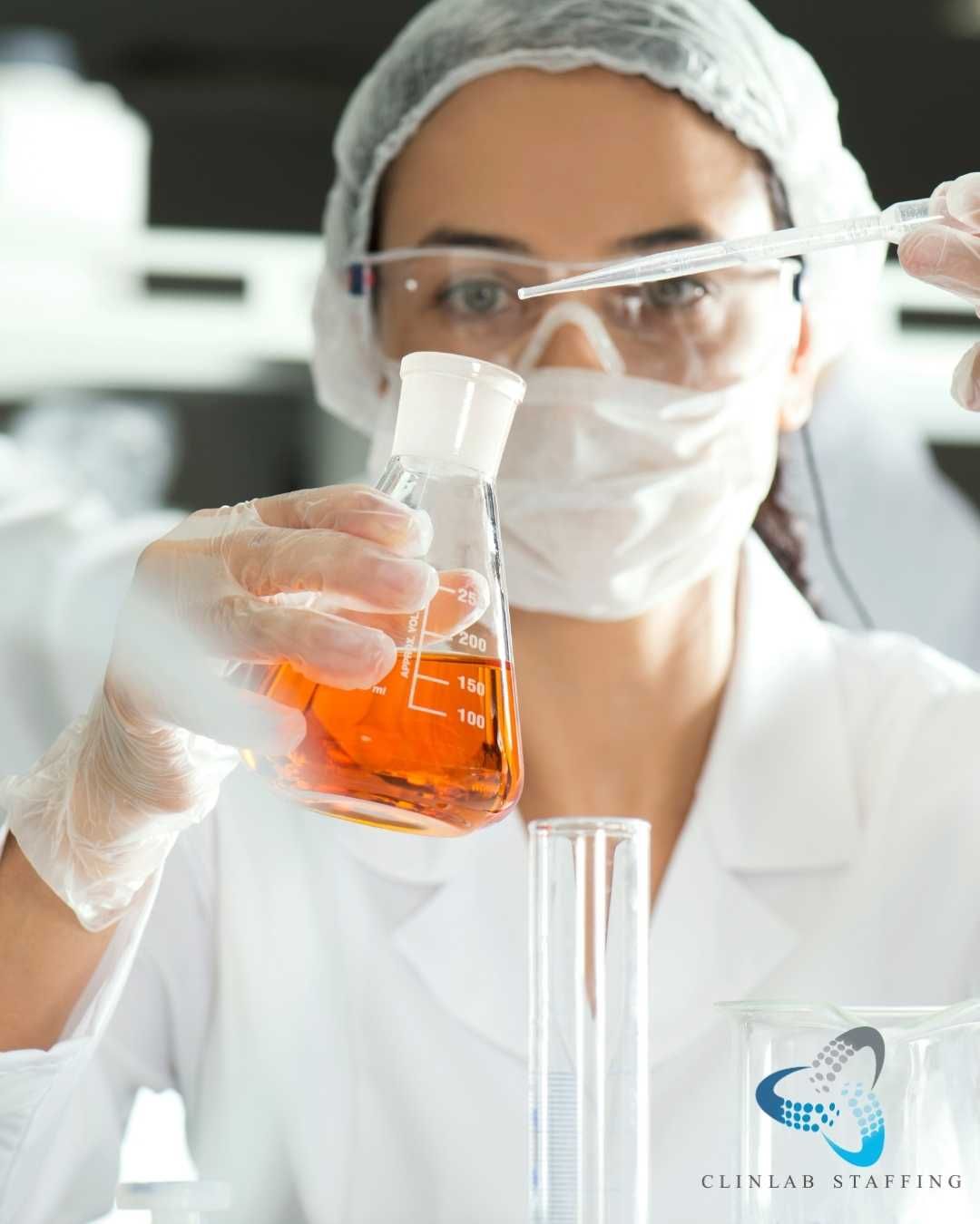 Scientist in lab coat and mask holding an orange liquid flask with a test tube nearby
