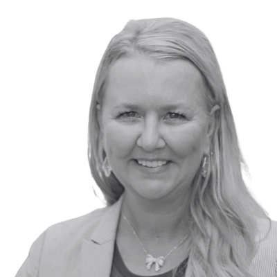 Headshot of a smiling person with long light hair, wearing a blazer and necklace against a plain white background