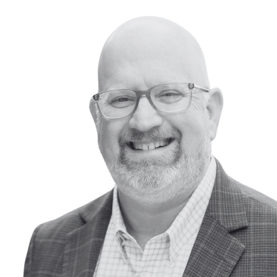Smiling bald man with glasses and a plaid blazer against a white background