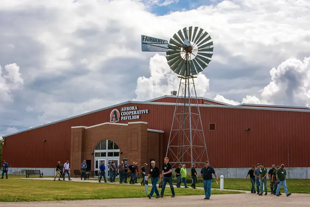 Red barn-like building with a windmill and a crowd gathered outside under cloudy skies