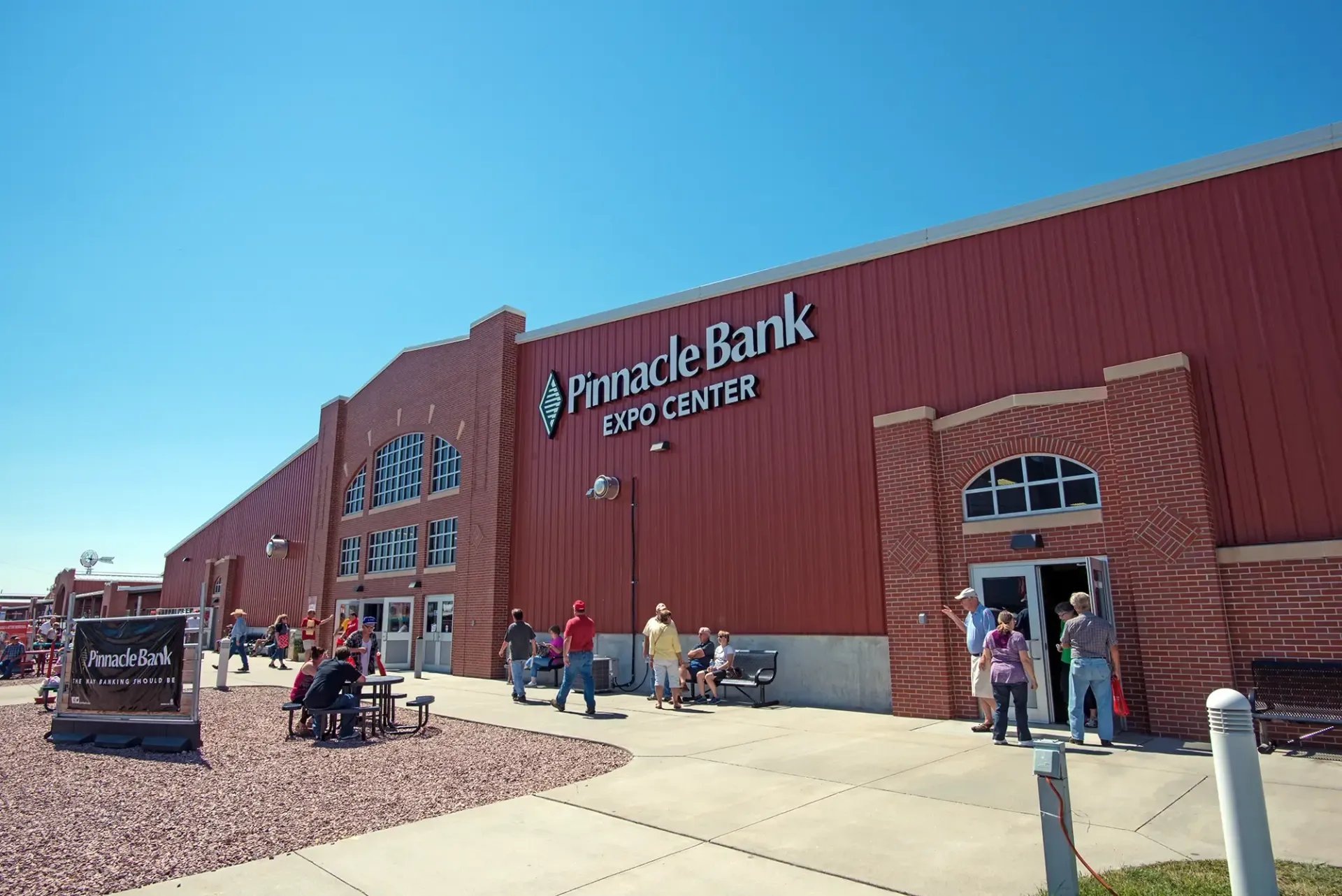 People entering Pinnacle Bank Center, a red arena building on a sunny day