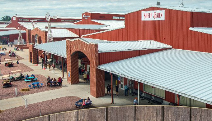 Outdoor shopping plaza with red buildings, white roofs, brick walkway, and a supermarket sign.