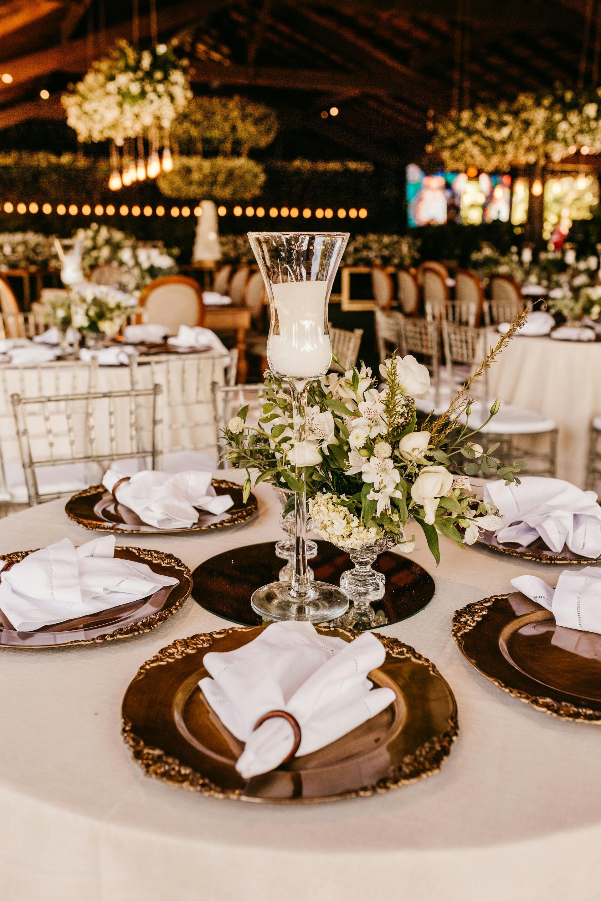 Elegant wedding reception table with gold chargers, folded napkins, white florals, and candlelit decor
