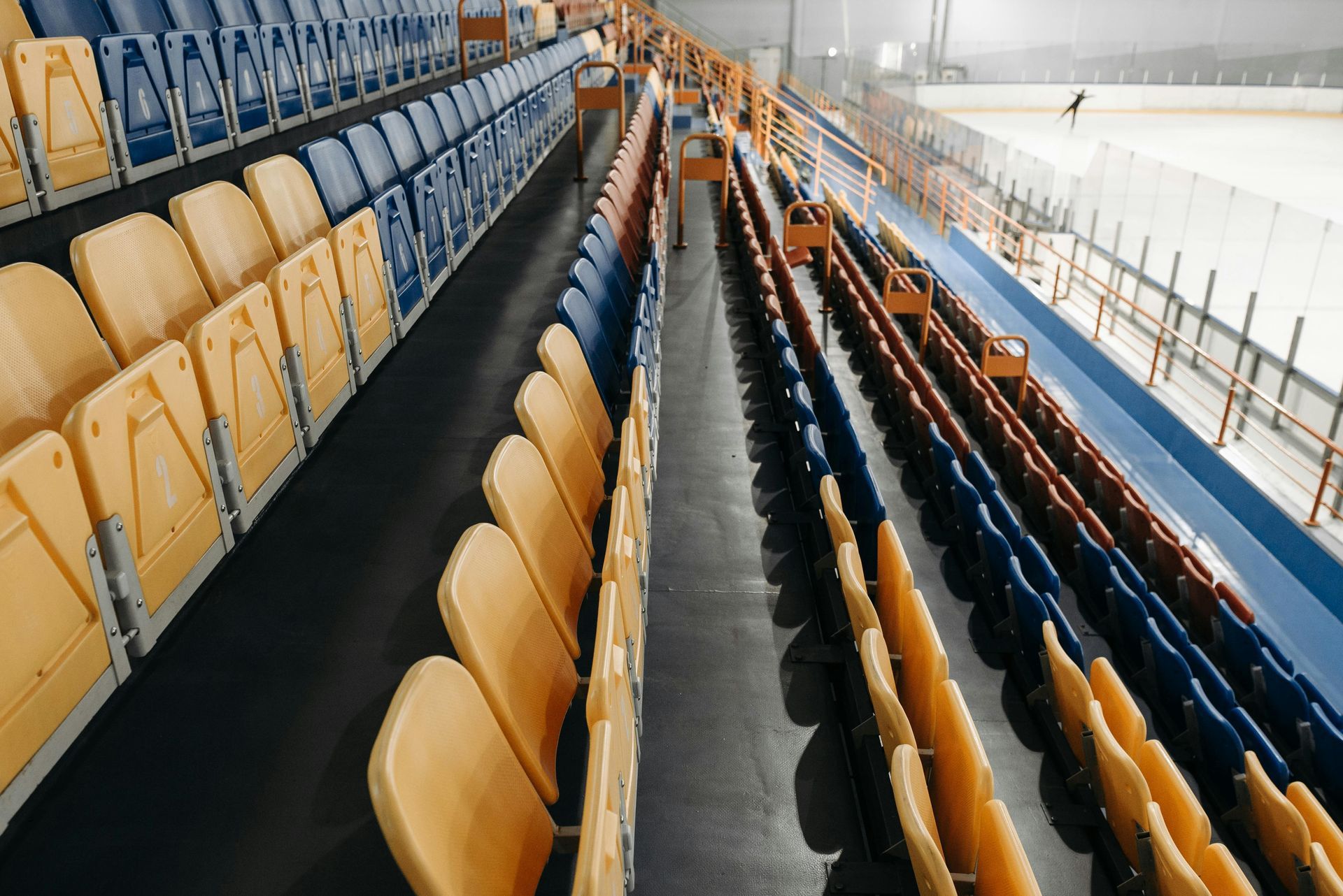 Empty indoor sports arena seating with rows of yellow and blue seats beside the ice rink