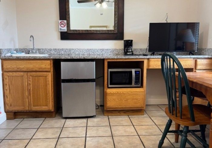 Hotel room kitchenette with granite counter, mini fridge, microwave, sink, mirror, and chair by tiled floor