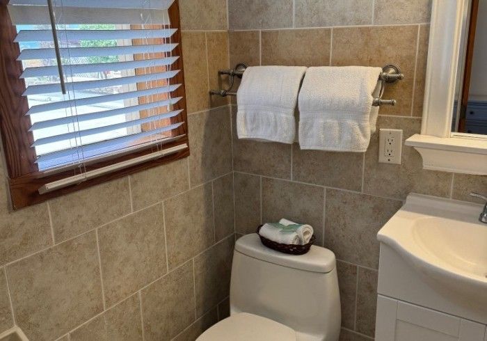 Bathroom with tiled walls, window blinds, towel rack, toilet, and sink vanity.