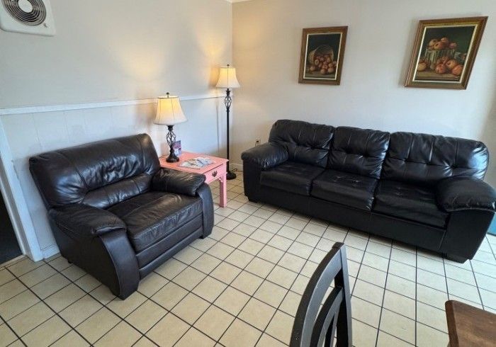 Living room with black leather couches, pink side table, lamp, and tiled floor