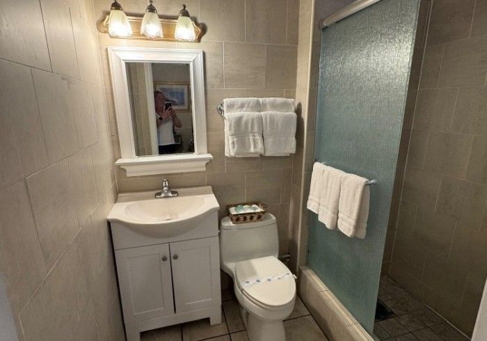 Small bathroom with white vanity, toilet, frosted shower, and towel rack beside a lit mirror.