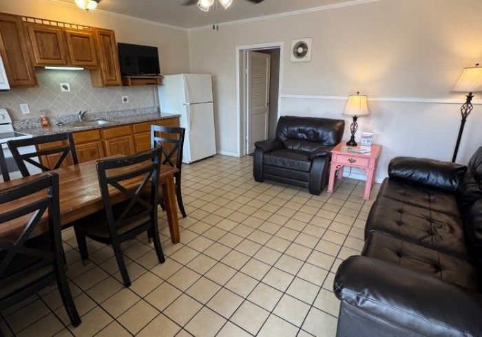 Small kitchen and living room with wood cabinets, black leather sofas, tiled floor, and a white fridge