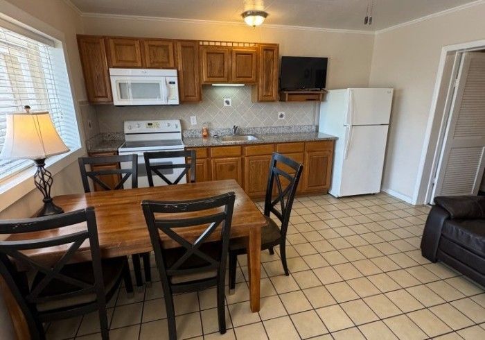 Compact kitchen-dining area with wooden table, tiled floor, cabinets, microwave, fridge, and sofa.