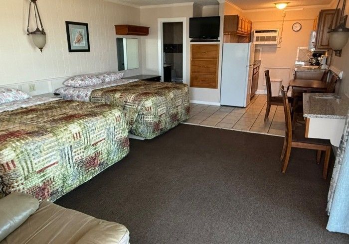 Motel room with two beds, desk, TV, and kitchenette on dark carpet.