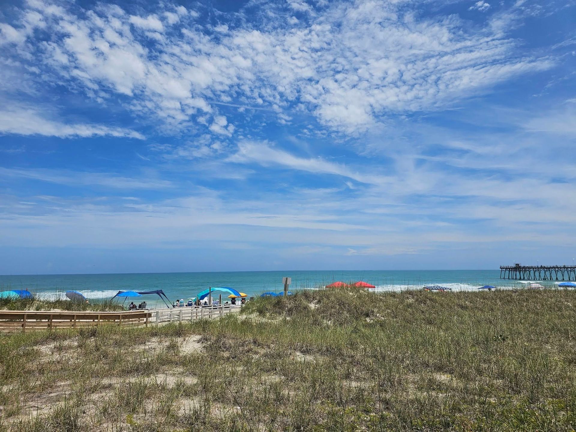 Beachfront with blue ocean, cloudy sky, and grassy dunes in the foreground