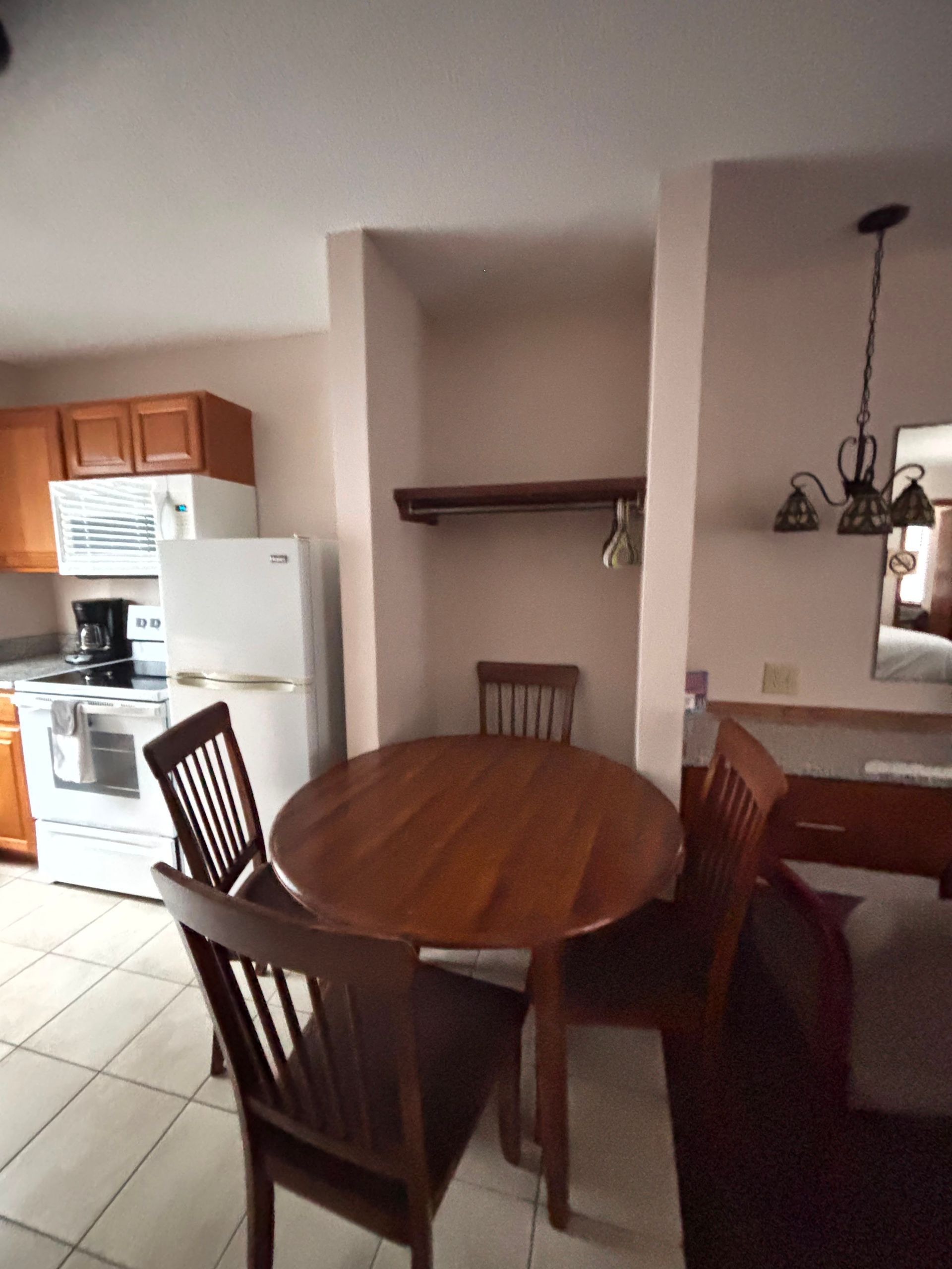 Dining area with oval wooden table and chairs beside a kitchen with white appliances