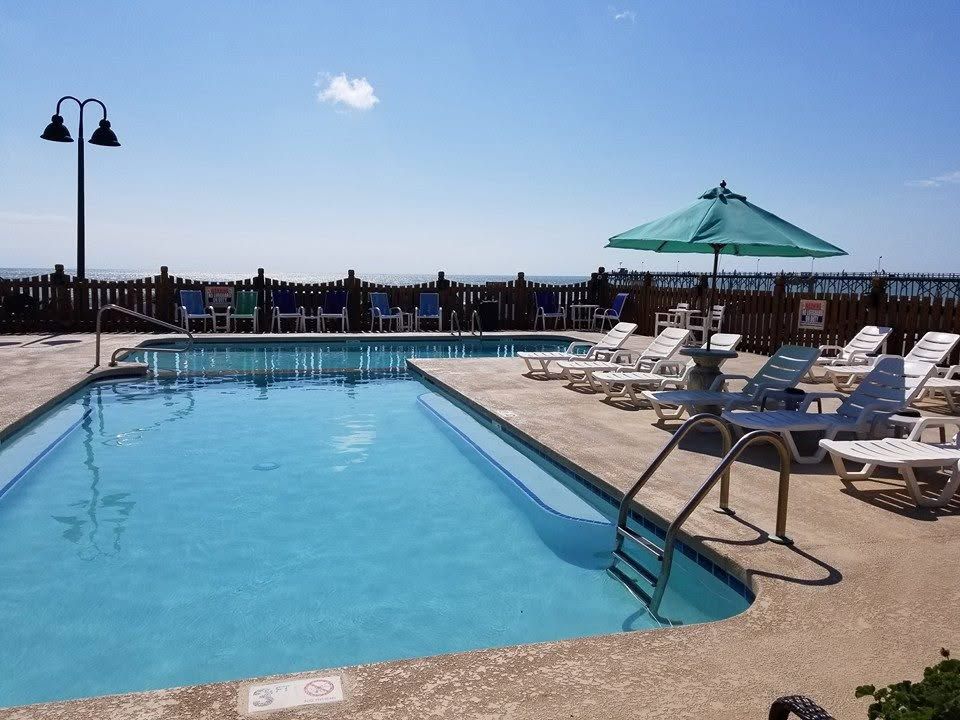 Outdoor swimming pool with lounge chairs, a green umbrella, and a clear blue sky