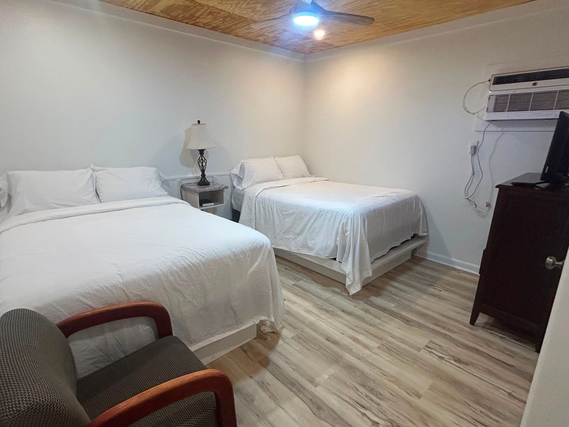 Small bedroom with two beds, chair, nightstand, dresser, and window air conditioner