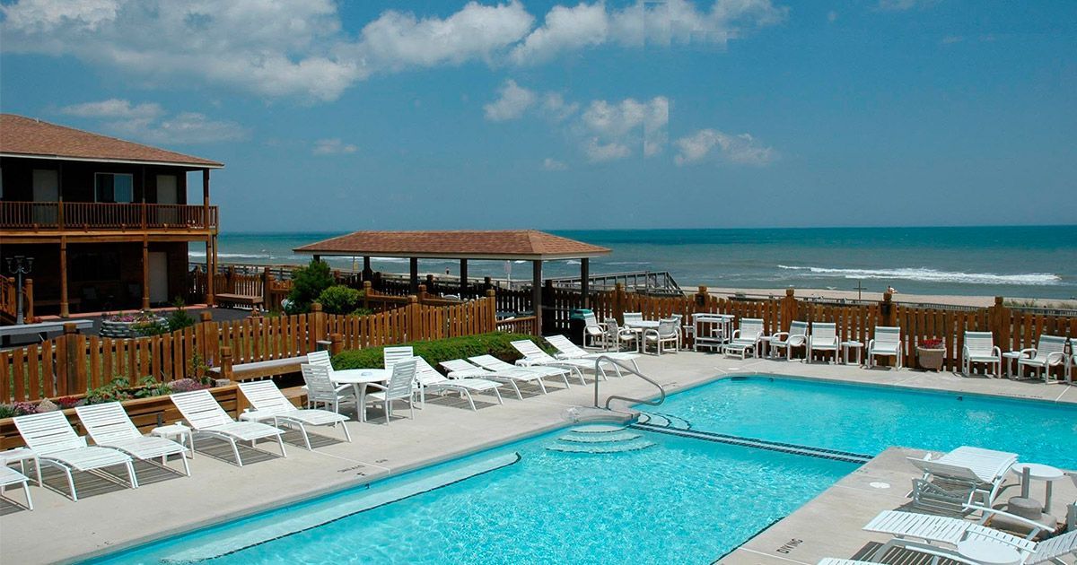 Resort pool with white lounge chairs beside the ocean under a blue sky