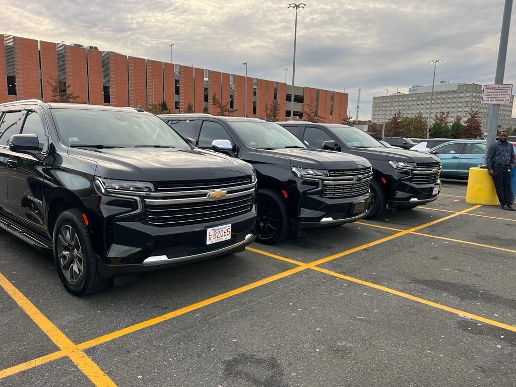 Three black Chevrolet Tahoe SUVs parked side-by-side in a large outdoor parking lot near a brick building.