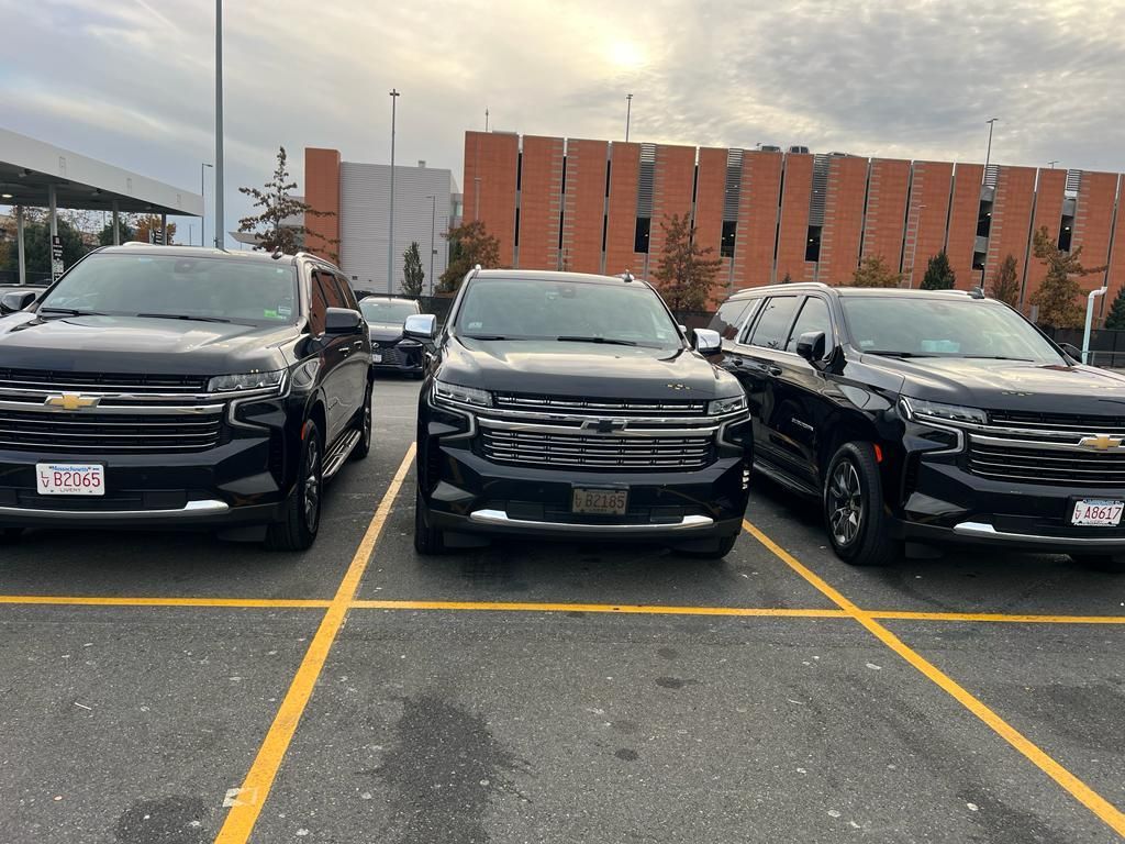 Three black Chevrolet SUVs parked in a row on an outdoor asphalt lot in front of a red brick parking garage.