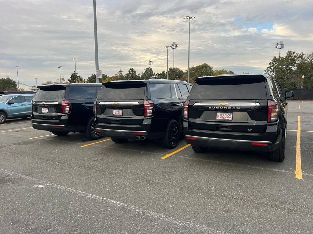Three black SUVs parked in a row in an outdoor parking lot under a cloudy sky.