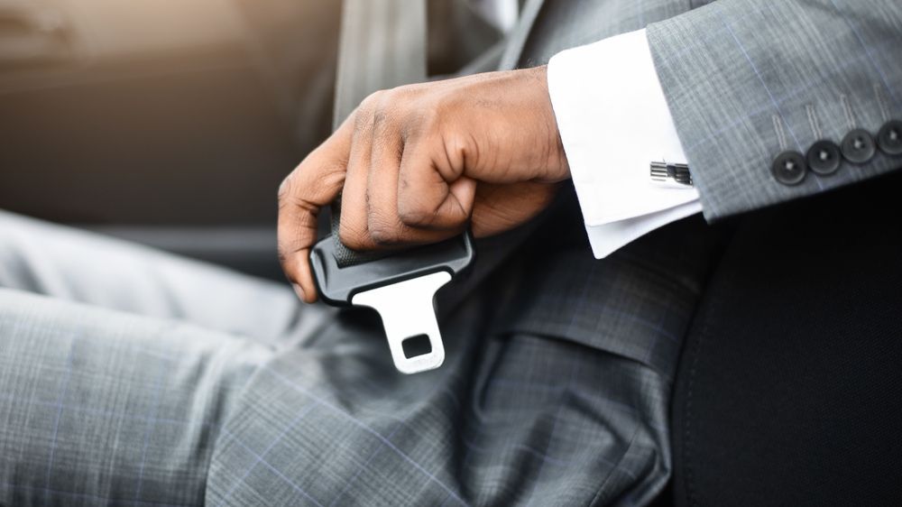 A person wearing a grey suit jacket and white shirt cuff clicks a car seat belt into place.
