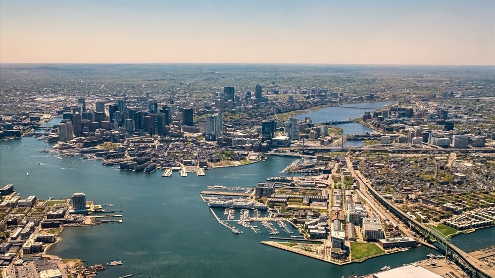 Aerial view of the Boston skyline and harbor, featuring coastal city buildings, bridges, and surrounding water.