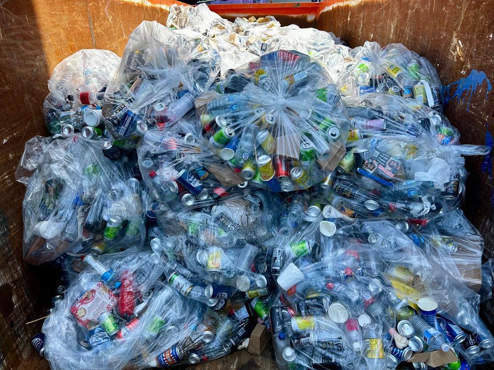 Bags of crushed aluminum cans fill a metal container, ready for recycling.