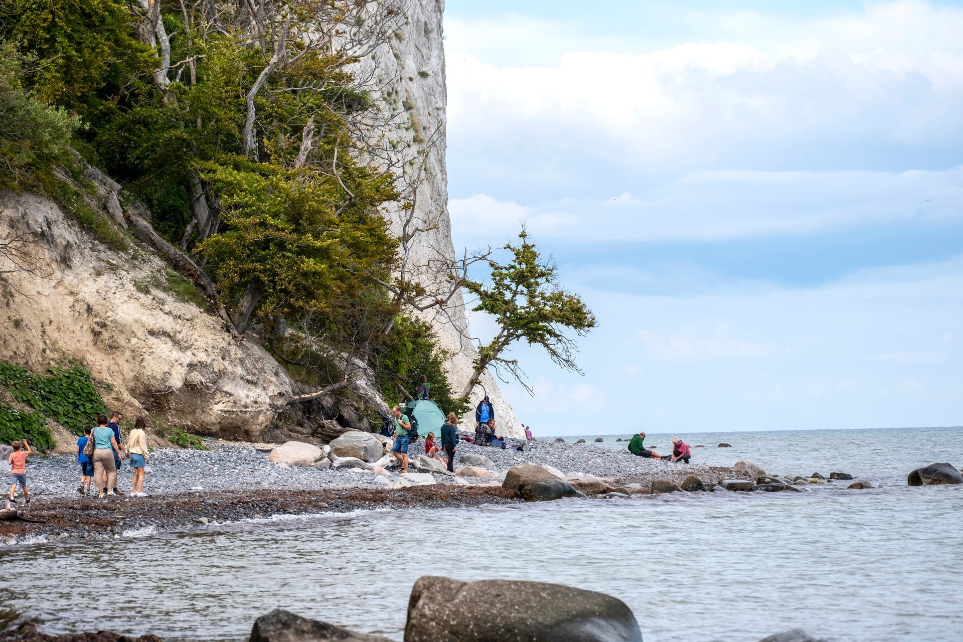 Folk på en klippefyldt strand under en klippe ved havet under en overskyet himmel