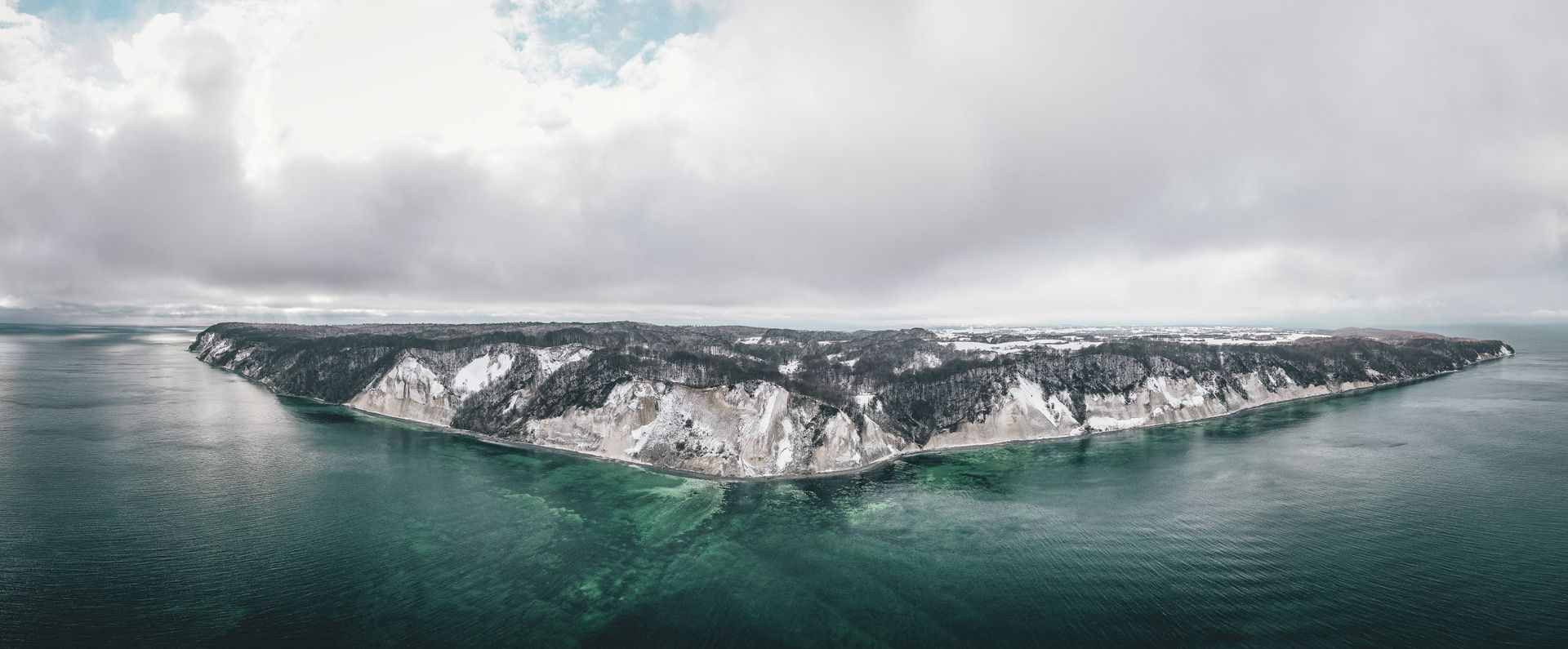 Snedækket kystlinje med hvide bølger under en overskyet himmel