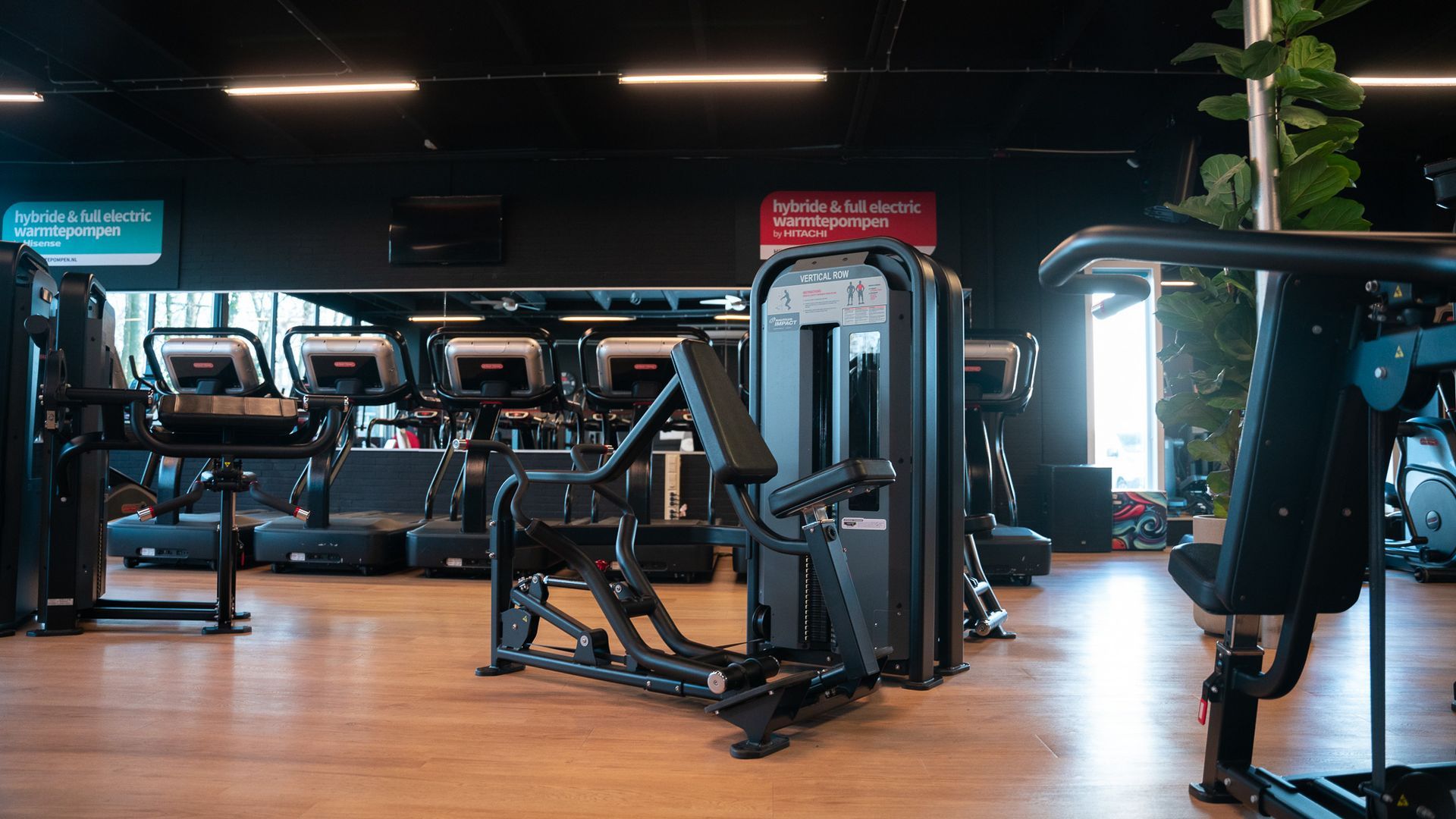 Interieur van een sportschool met gewichtenmachines en loopbanden op houten vloeren.