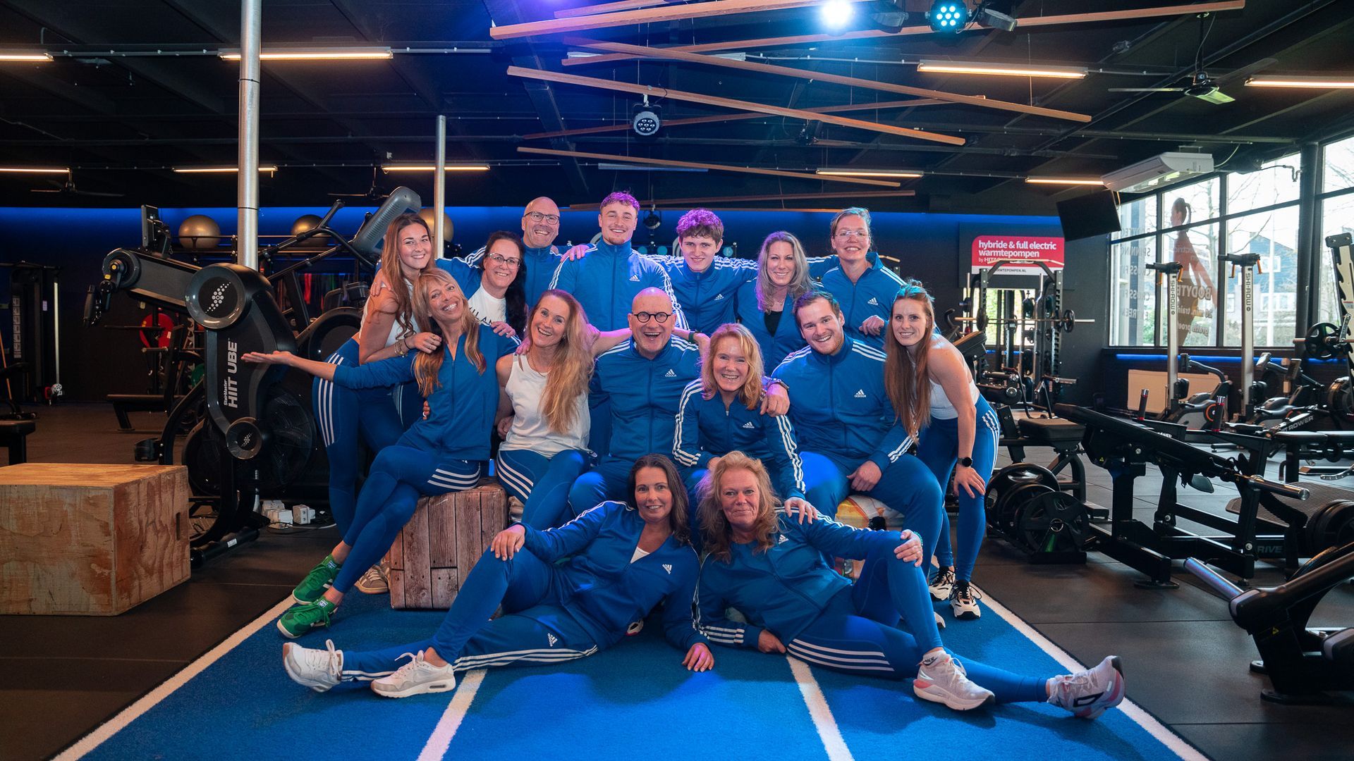 Een groep mensen in blauwe trainingspakken poseert in een sportschool.