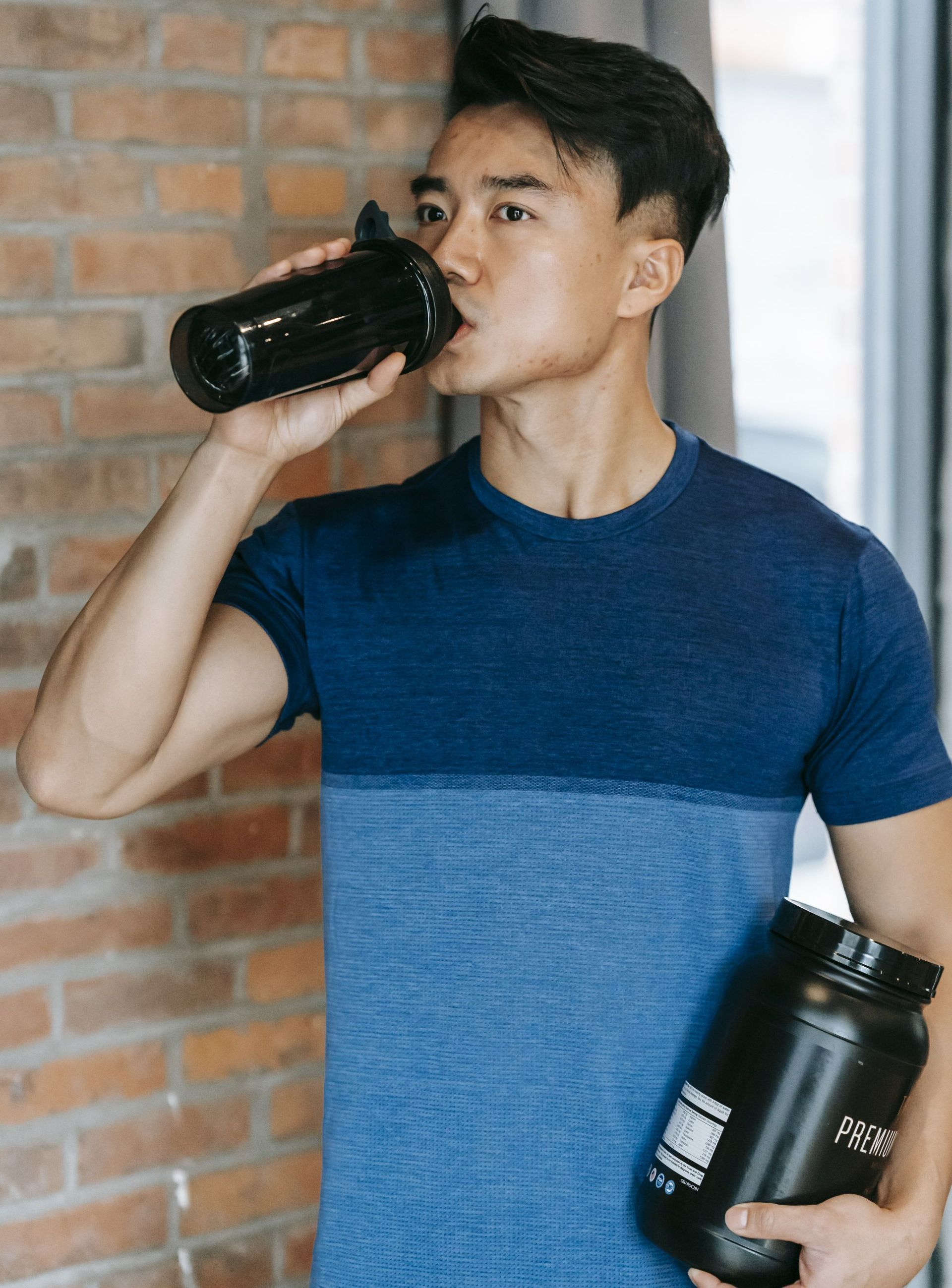 Een man drinkt water uit een fles terwijl hij een shaker vasthoudt.