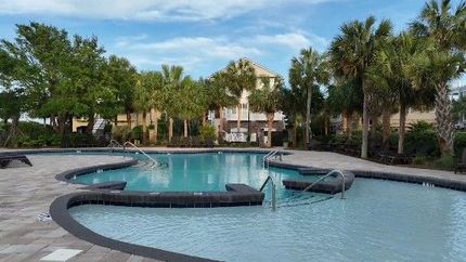 A large swimming pool surrounded by palm trees and a building.