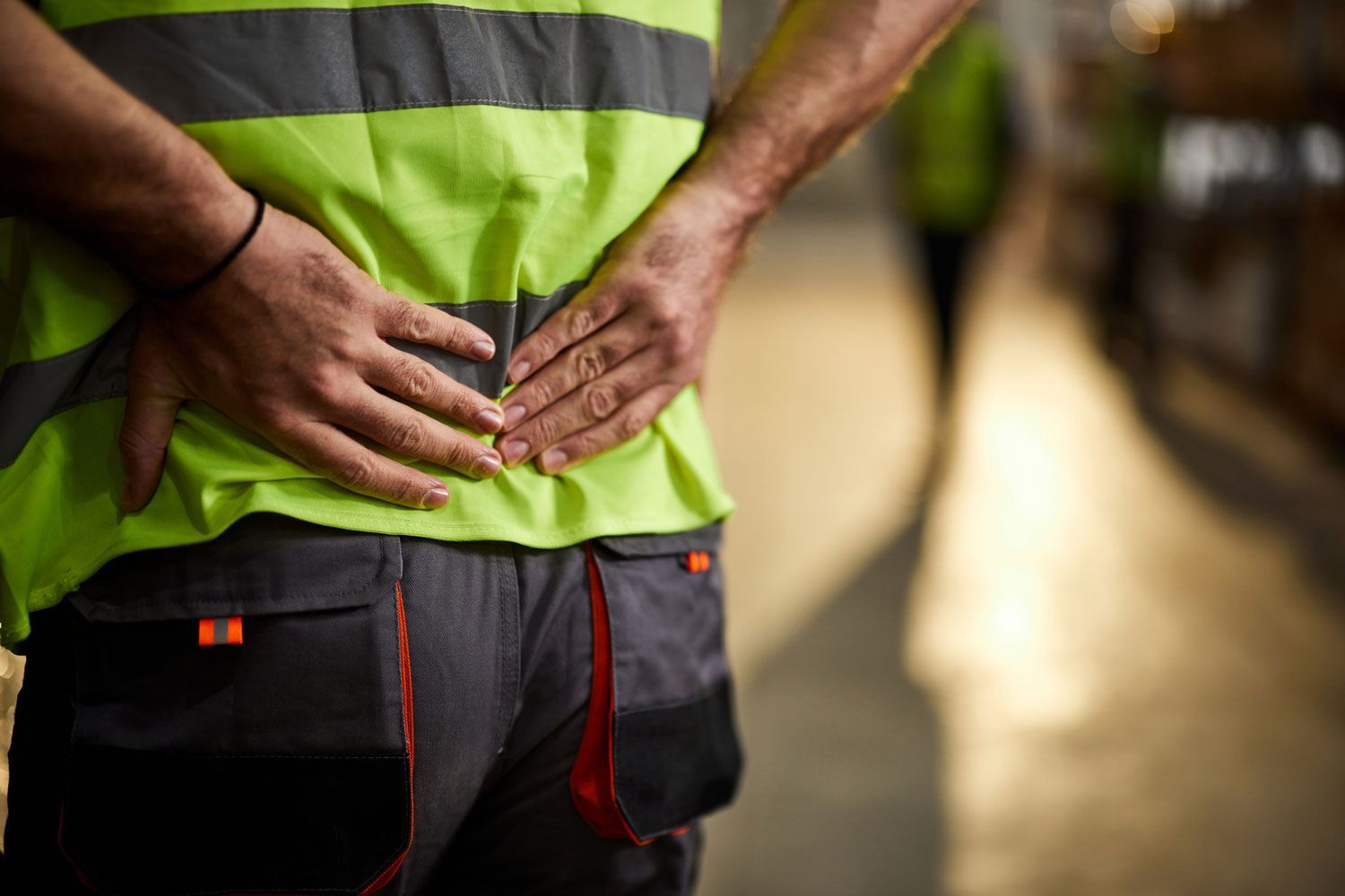 A man is holding his back in pain while wearing a safety vest. A man is holding his back in pain while wearing a safety vest.