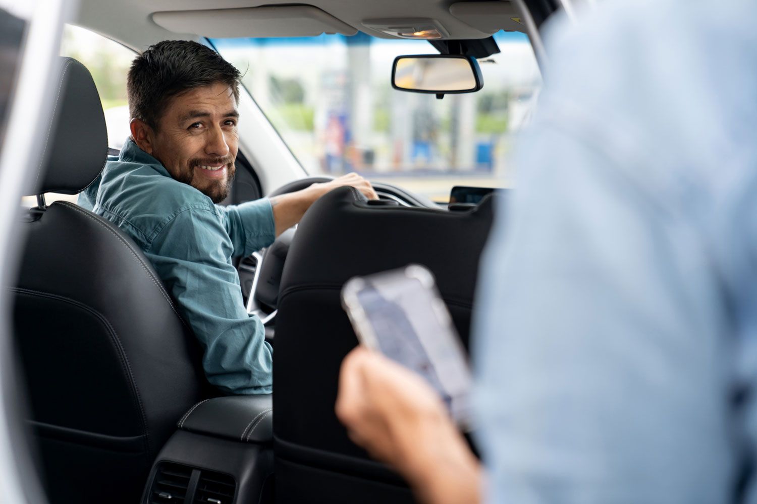 A man is sitting in the back seat of a car while a woman is holding a cell phone.