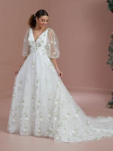 Woman in white wedding dress with floral accents and long train, smiling.
