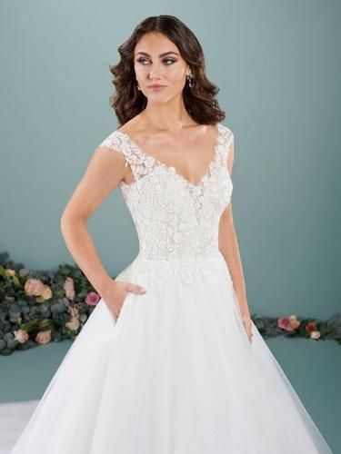 Woman in a white wedding dress with lace bodice, pockets, and a flowing skirt, looking to the side.