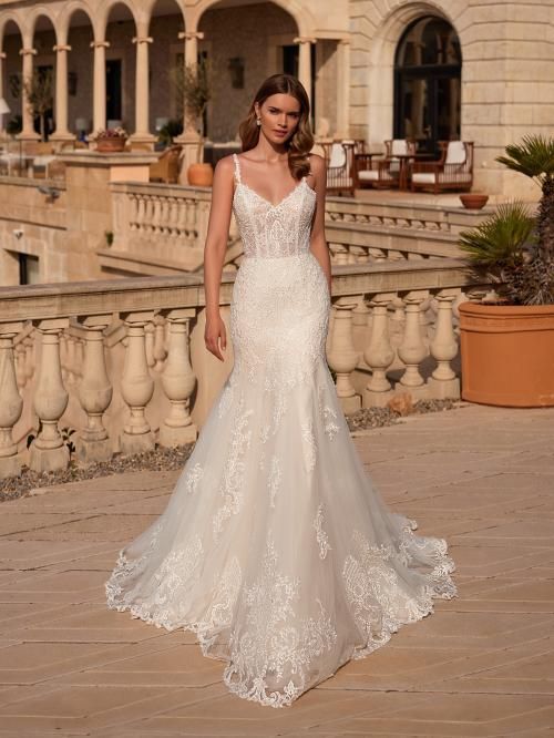 Woman in a white lace mermaid wedding dress on a stone patio with a palatial backdrop.