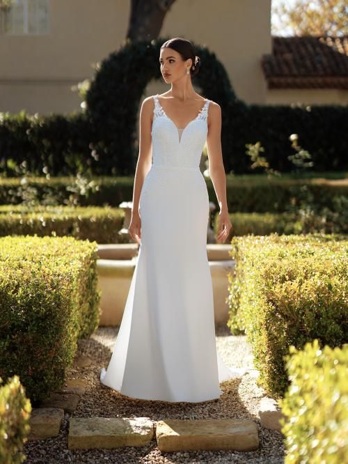 Woman in white wedding dress walking outdoors in a garden.