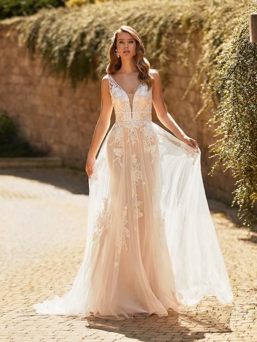 Woman in a wedding dress with lace detailing, standing outdoors with a flowing skirt, posing gracefully.