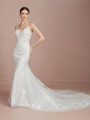 Bride in a white lace mermaid wedding dress with a long train, standing against a pink wall.