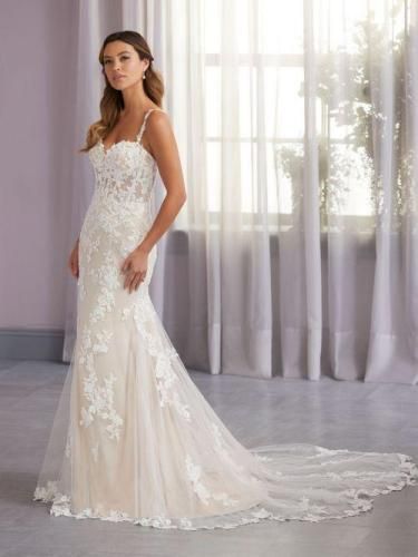 Woman in a white, lace mermaid wedding dress with a train, standing near a window.