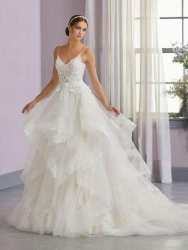 Woman in white wedding dress with layered skirt, standing in a well-lit room.