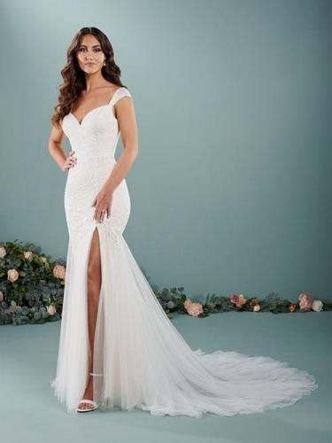 Woman in white wedding dress with a thigh-high slit, posing in front of a blue background.