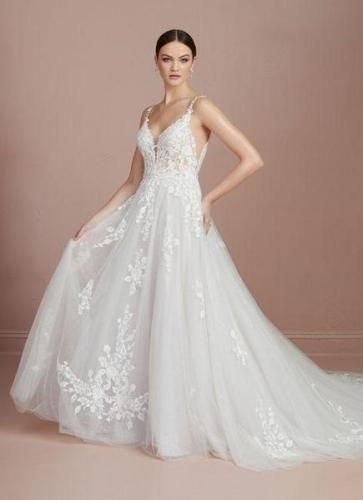 Woman in white wedding dress, floral lace, scoop neckline, hands on hips, posing.